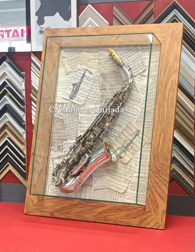 Saxo antiguo enmarcado en urna de cristal Saxofón enmarcado sobre fondo de hojas de papel en una pared decorativa.