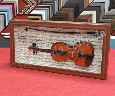 Violín enmarcado. Violín enmarcado con arco, colocado sobre un fondo de partituras, y con puerta de fácil acceso.